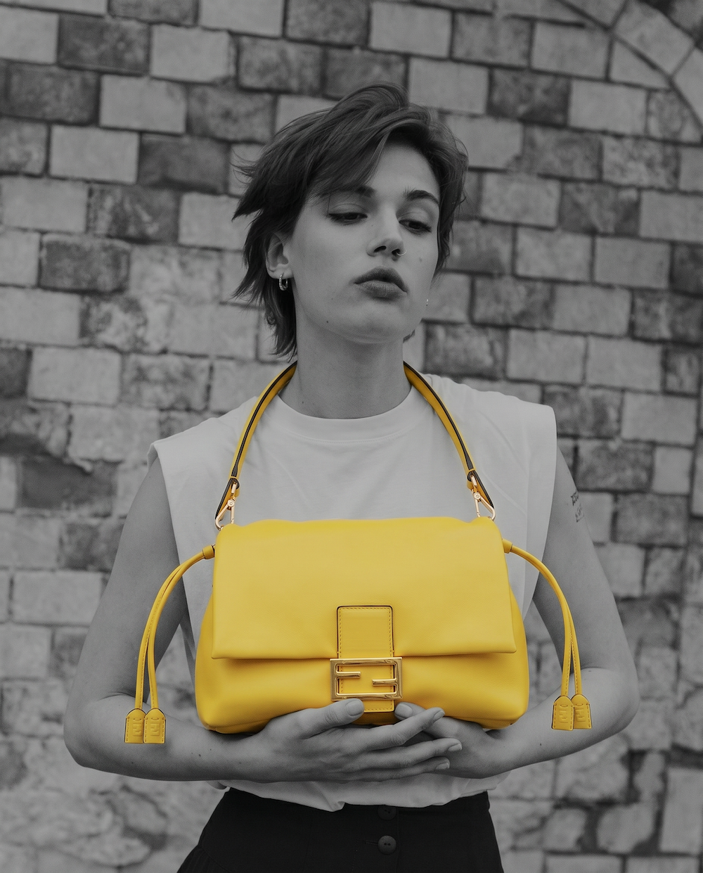 Model holding a yellow leather baguette bag against a stone wall